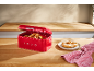 Red bread bin with pretzels and a pretzel on a plate on a wooden table.