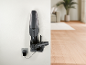 Black cordless handheld vacuum cleaner mounted on wall, charging, in a modern interior.