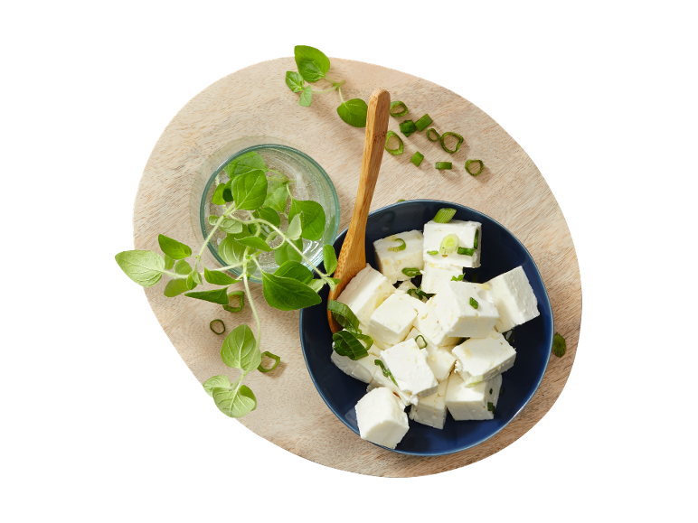 Feta cheese cubes with fresh oregano and chopped spring onions on a wooden board.