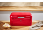 Glossy red bread bin on a wooden countertop with a sandwich and a cloth.