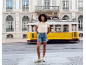 Woman in a beige T-shirt and denim shorts in front of a moving yellow tram.