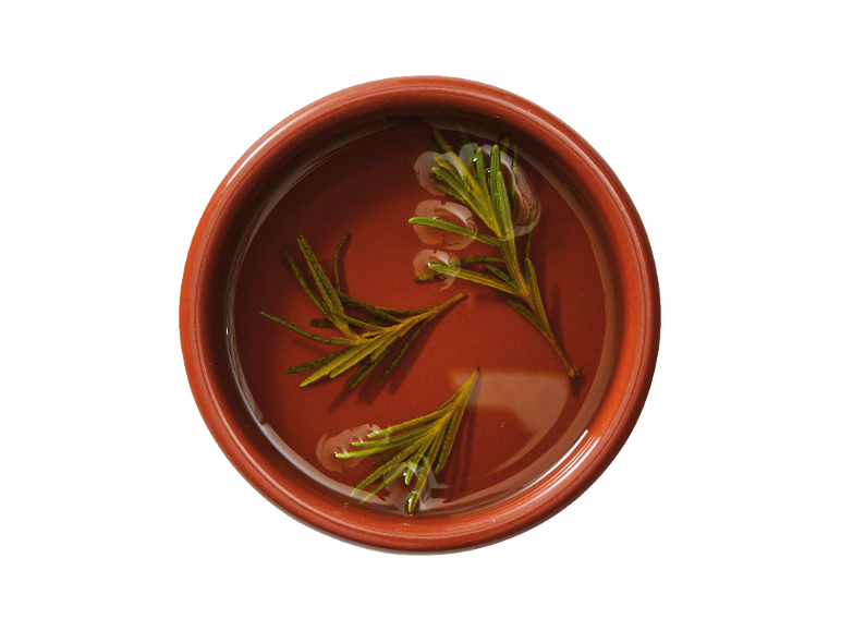 Fresh rosemary sprigs floating in olive oil in a terracotta bowl.