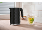 Black hexagonal pattern kettle and steaming mint tea cup on a wooden countertop.