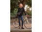 Woman in a black pea coat and jeans, standing with a bicycle in a park.
