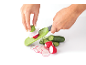 Hands using a mandoline to slice radishes and cucumbers.
