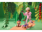 Girl with helmet on a scooter, next to a plush dog, in a jungle-like setting.