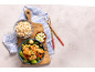 Bowl with chicken, broccoli, and carrots, with brown rice and green onions, with chopsticks.