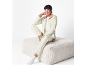 Woman in beige tracksuit and white t-shirt, sitting on a white ottoman.