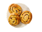Three golden-brown pain aux raisins on a white plate against a black background.