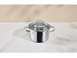 Stainless steel pot with a glass lid on a white countertop.