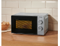Silver microwave oven on a wooden countertop with a basket of bread slices.