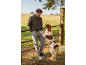 Man in bomber jacket and cargo pants with a dog in a field.