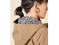 Woman in a beige hooded raincoat with a hoop earring, side view.
