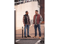 Two men in plaid shirts, jeans, and puffer vests standing outdoors.