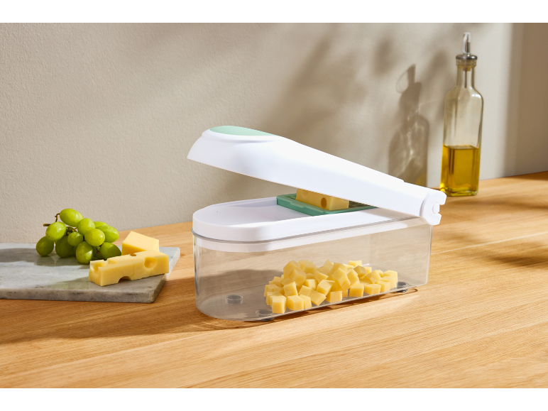 Cheese cutter with cubed cheese, grapes, and oil on a wooden table.