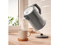 Grey electric kettle pouring hot water into a mug on a wooden countertop.