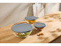 Three glass bowls with grey lids, filled with salad, lemons, and pretzels.