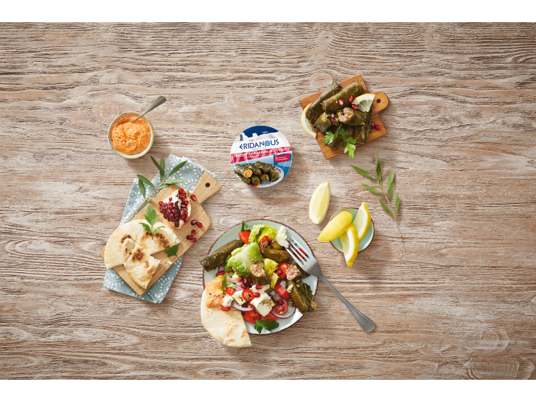 Greek-style stuffed vine leaves with rice, salad, bread, and dip on a wooden table.