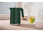 Dark green kettle with hexagonal pattern and steaming mint tea cup on a wooden countertop.