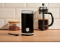 Black coffee grinder, glass coffee jar, and French press on a wooden table