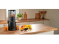 A black slow juicer on a kitchen counter, with fresh juice and fruit.