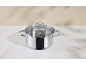 Stainless steel pot with glass lid on a white marble surface.