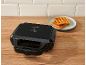 Black waffle maker with two golden waffles on a plate on a wooden surface.