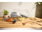 Glass food storage containers with grey lids, filled with salad, sauce, and olives.