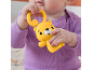 Baby in purple bodysuit holding a yellow bear-shaped rattle.