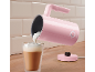 Pink milk frother pouring foam into a glass of latte on a wooden counter.