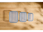 Three transparent food containers with blue lids on a wooden table.