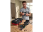 Man holding a cordless drill, with a tool case, battery charger, and bit set on a wooden table.