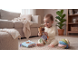 Smiling baby playing with a capybara plush toy and fabric toys in a cozy living room.