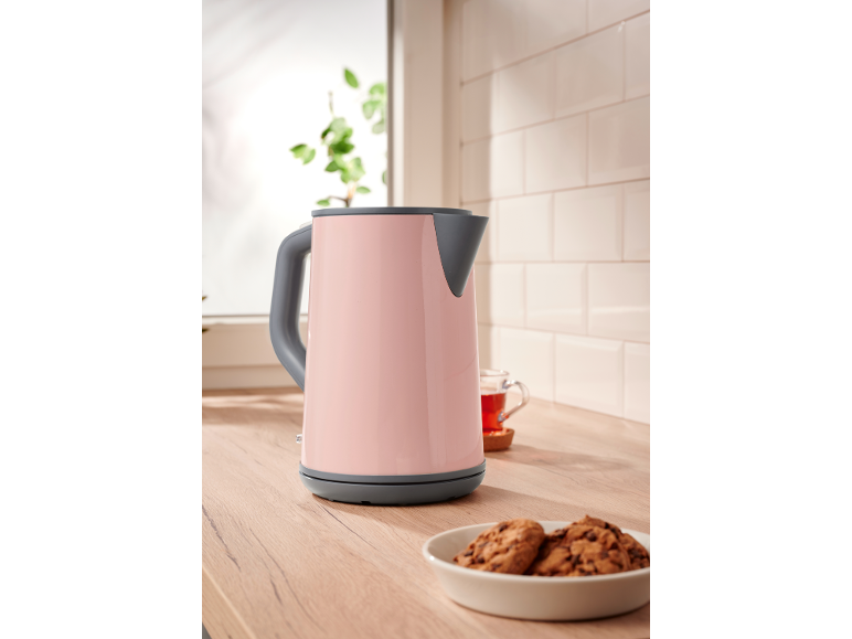 Pink electric kettle on a kitchen counter with cookies and tea.