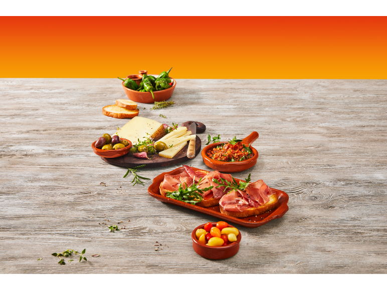 Cheese and charcuterie board with olives, padrón peppers, and bruschetta on a wooden table.