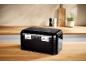 Black bread bin on a wooden kitchen counter with salt and pepper grinders and a plant.