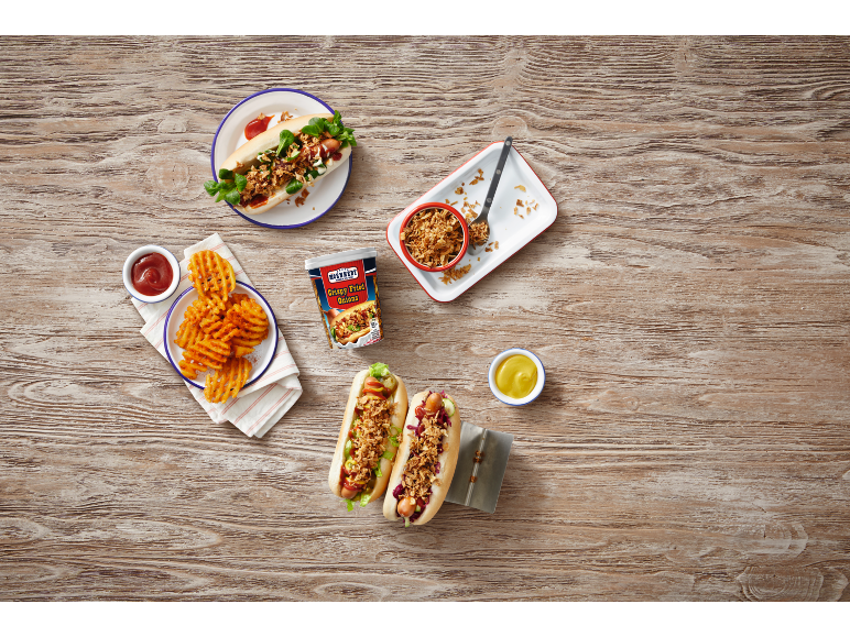 Two hot dogs with crispy onions, waffle fries, and a pack of crispy onions on a wooden table.