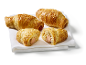 Four puff pastry sausage rolls with sesame seeds on a white cloth, two of them cut.