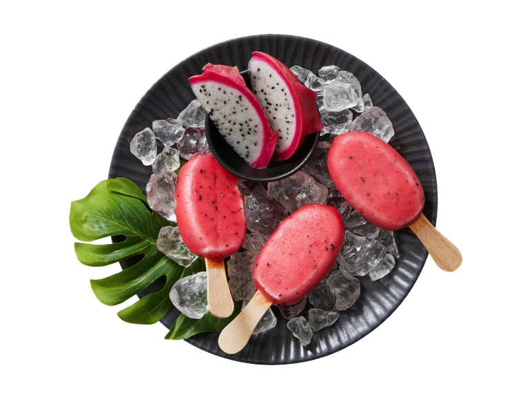 Red dragon fruit popsicles with ice and sliced dragon fruit on a dark plate.