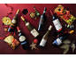 Several bottles of red and white wine with glasses, appetizers, and festive decorations on a red background.