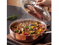 Man smiling at steaming vegetable stew in a copper pot with a glass lid.