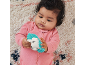 Baby in pink sleepsuit holding a hedgehog teether on a patterned rug