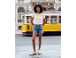 Woman in embroidered t-shirt and denim shorts in front of a yellow tram.