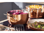 Copper pots with cooking vegetables and a pan with mushrooms on an induction hob.