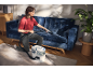 Woman cleaning a blue sofa with a washing vacuum cleaner in a living room.