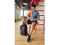 Man in sportswear sits on a stool with a towel and a backpack.