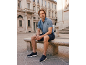 Man in blue polo shirt and dark shorts sitting on a stone bench.