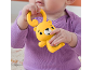 Baby in purple bodysuit holding a yellow bear-shaped rattle.