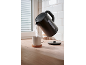 Black electric kettle pouring hot water into a mug on a wooden counter.