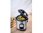 Stainless steel rice cooker with steamed vegetables on a wooden countertop.
